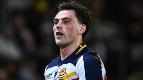 Head and shoulders of Catalans Dragons player Lewis Dodd, in white and dark blue strip with yellow and red trim.