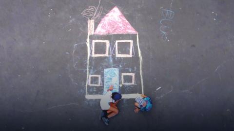 An ariel view of two children drawing a house using chalk.