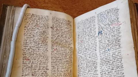 The 14th Century manuscript with Latin text lies open and has a white rope book mark inside one of its pages