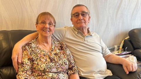 Marilyn and Michael sit on black leather sofa smiling