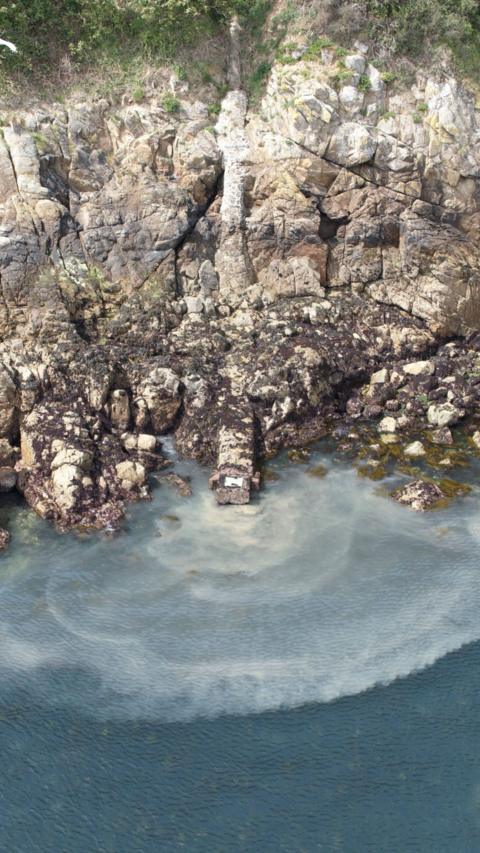 Raw sewage being discharged into the sea from a pipe down a cliff face