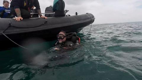 A man in a diving suit smiles as he bobs in the sea by a power boat.