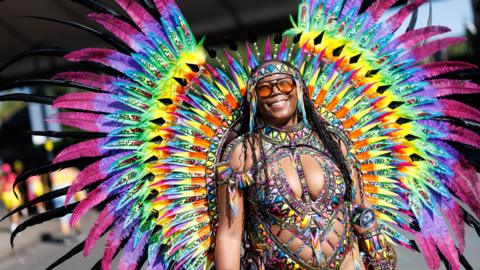A woman wears a rainbow coloured costume with feathers fanning out behind her.