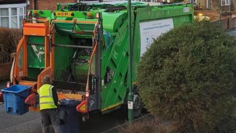 A refuse worked loading a wheelie bin onto the back of a lorry