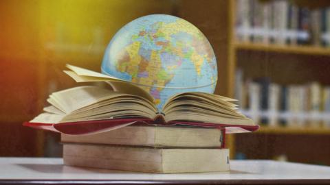 A stack of books in front of a globe map of the Earth