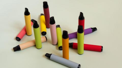 An assortment of multicoloured vapes arranged on a white surface.