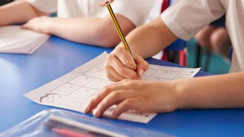close crop of the hands of a child working in class on a worksheet with a pencil