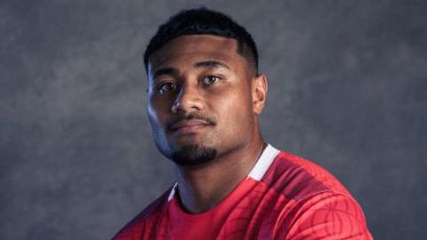 A portrait photo of Sam Moli in a red Tonga rugby jersey.
