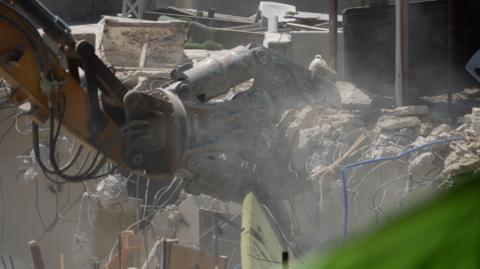 An excavator picks up rubble and wires after the demolition of a building.