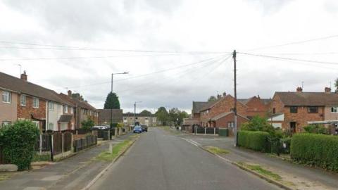 A suburban road with a pavement on either side and a mix of terraced and semi detached homes