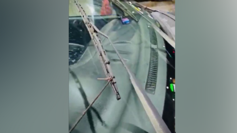 A close-up of a car windscreen and it's wipers. The closest wiper is tied to what appears to be a black shoe lace.