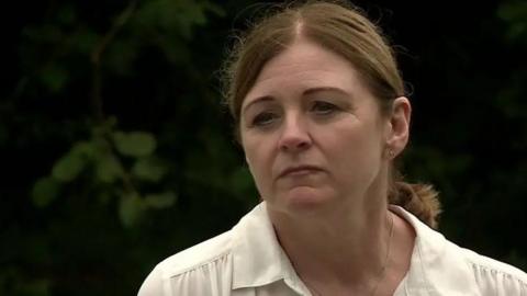 Debbie Adlam wearing a while blouse, in front of a dark background of shrubs