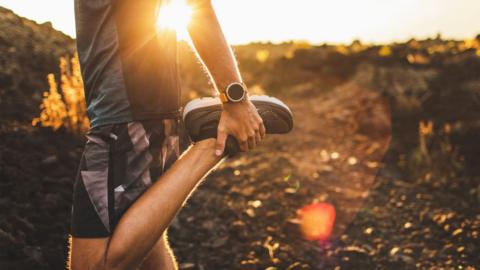 A man stretches in exercise clothing in the early morning sunlight 