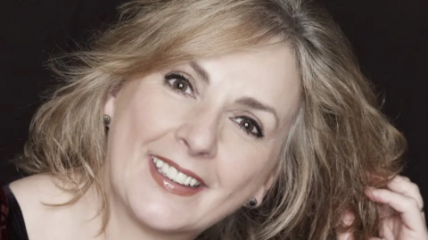 A close up image of Moya Brennan smiling at the camera. She has blonde hair and brown eyes.
