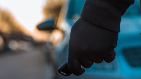 Black gloved hand holding a key fob in front of a blurred car