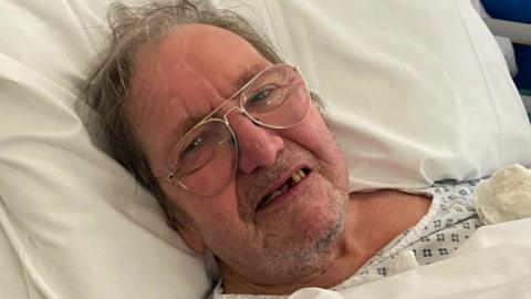 Mr Sexton, a man wearing glasses laying in a hospital bed.