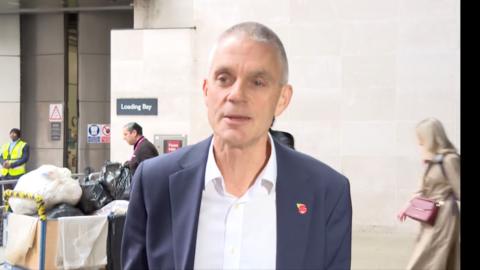 Tim Davie wearing a navy blue suit jacket and a white shirt.