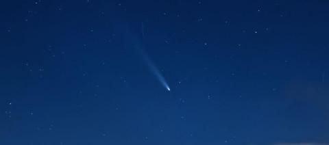 A comet appears as a glowing, streaking dot against the vast, dark, night sky