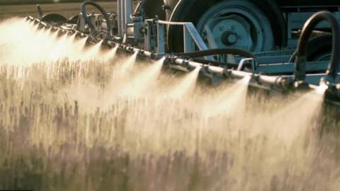 A close up shot of herbicides from the back of a farm vehicle being applied to crops 