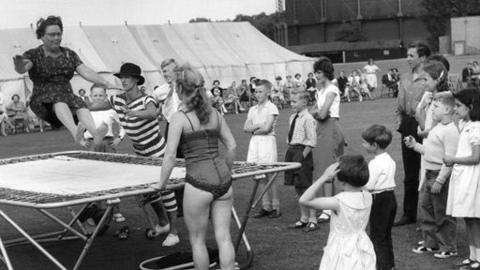 Holiday makers watch a woman on a trampoline.