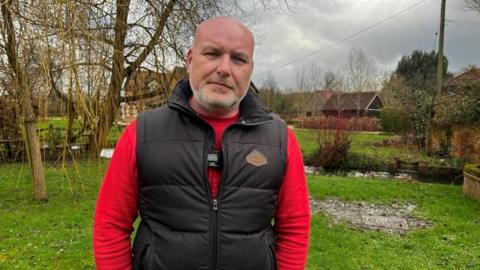 James is wearing a red long sleeve top and black vest 