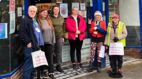 Exterior of the Wycombe Food Hub community shop, showing a group of volunteers standing outside the entrance beneath the organisation’s signage on the High Street.
