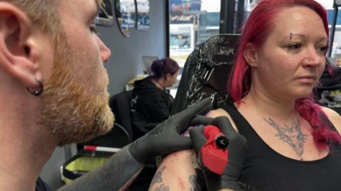 A woman with pink hair having a tattoo done. 