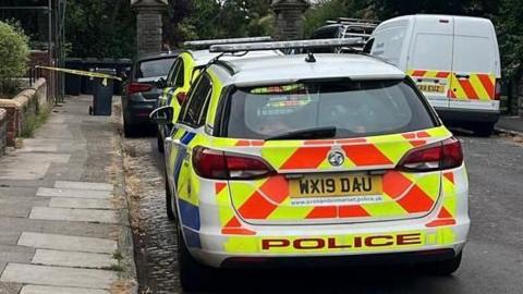 A parked police car on a residential road, with a yellow cordon in the background