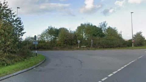 A view of the junction on the A4061 near Great Saredon, where Saredon Road meets Wolverhampton Road in Cannock. There are road signs and road markings and lampposts and grassy verges with shrubs and trees.