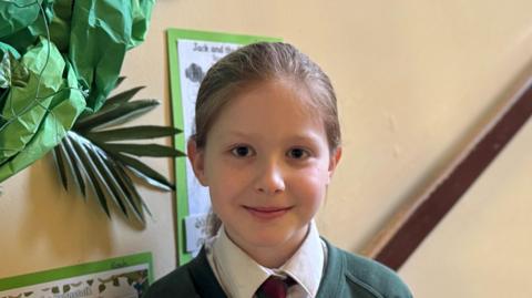 Child is smiling at camera, she is in her school hallway.