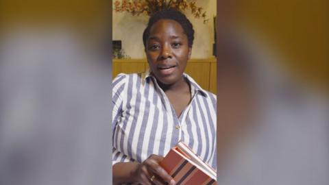 Kimberley Wilson wearing a white and blue striped shirt holding a notepad.