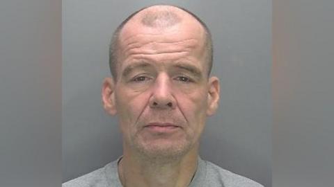 Terry Lewis in custody, appearing bald and wearing a grey jumper