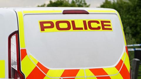 A generic photo of the back of a police van which has yellow and orange markings. 