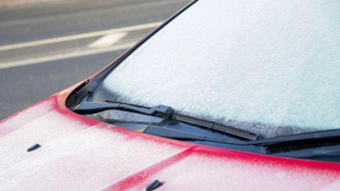 A red car with its windscreen covered in frost.