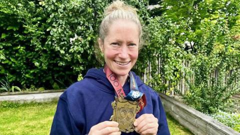 Anna Rutherford holding large gold medal with ga4rden backdrop 