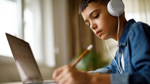 Teenage boy sitting at a laptop studying with headphones on