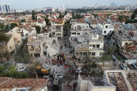 An aerial photo shows rescue teams standing among rubble in a suburban area