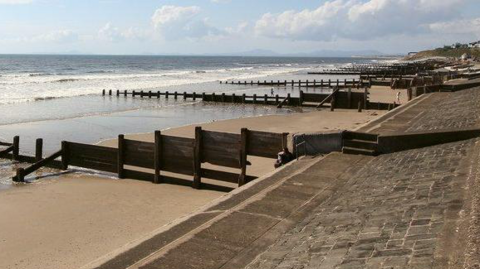 Barmouth beach, show beach defences and the sea out a little with small waves washing onto the sand