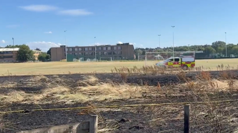 A large area of burnt grassland near a school playing field, with a fire vehicle near it.