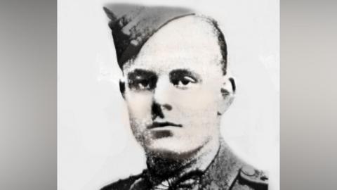 A black and white image of a man with short dark hair, wearing a naval uniform hat. He appears against a whitebackground.