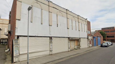 A derelict white building with its shutters down on a street.