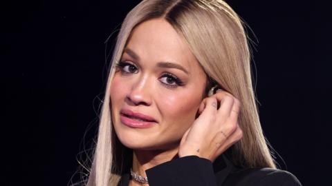 Rita Ora holds her ear piece as she becomes emotional paying tribute to Liam Payne