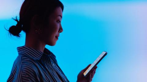 A woman in a striped shirt looks at a phone screen.