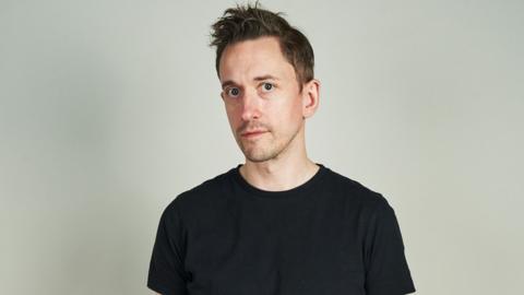 John Robins wearing a dark t-shirt and looking at the camera