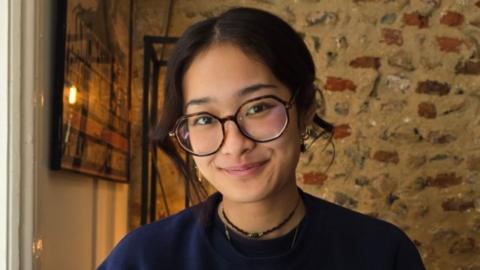 Woman with dark hair and glasses smiles at camera