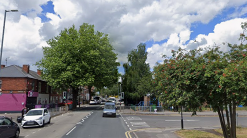 A stock image of a road, with a junction to the right. There are cars on the left and more in the background, with several trees lining the road