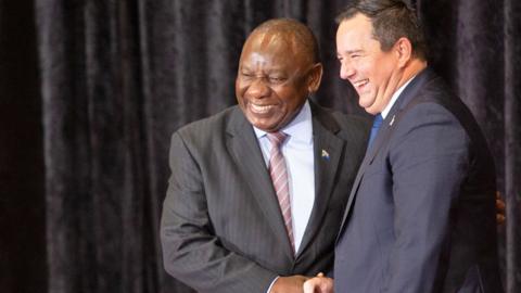A smiling President Cyril Ramaphosa shakes hands with John Steenhuisen of the Democratic Alliance - who is also smiling