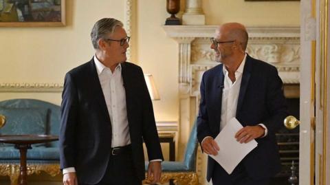 Two men (Sir Keir Starmer and Nick Robinson) look at each other as they walk through a doorway