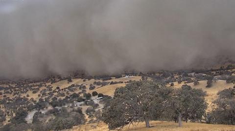 A huge cloud of dust sweeps over fields and trees.