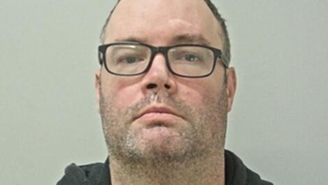Thomas Freret has dark-framed glasses, stubble and short dark hair.